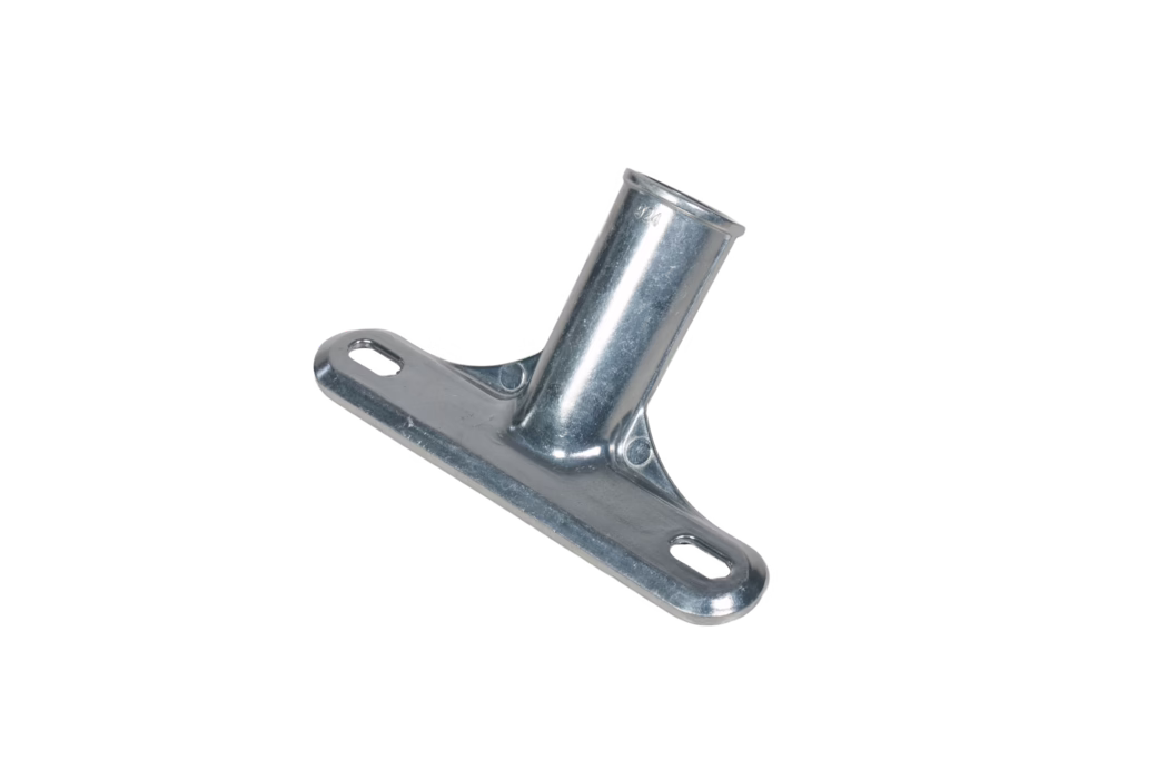 Nahaufnahme einer verzinkten, schräg gestellten Metallbefestigung. Das Bauteil hat eine flache, rechteckige Grundplatte mit zwei länglichen ovalen Montageschlitzen und eine angeschweißte zylindrische Hülse, die im Winkel zur Platte steht. Die Oberfläche zeigt eine helle, leicht strukturierte galvanisierte Beschichtung mit feinen Bearbeitungsspuren und einer kleinen Prägung in der Nähe der Hülse. Verstärkungsrippen verbinden Hülse und Grundplatte, abgerundete Kanten und Ausfräsungen dienen der Aufnahme von Befestigungselementen. Das Teil ist auf weißem Hintergrund fotografiert und ist dafür ausgelegt, ein Rohr oder eine Stange aufzunehmen und mittels Schrauben oder Bolzen durch die Schlitze zu befestigen.