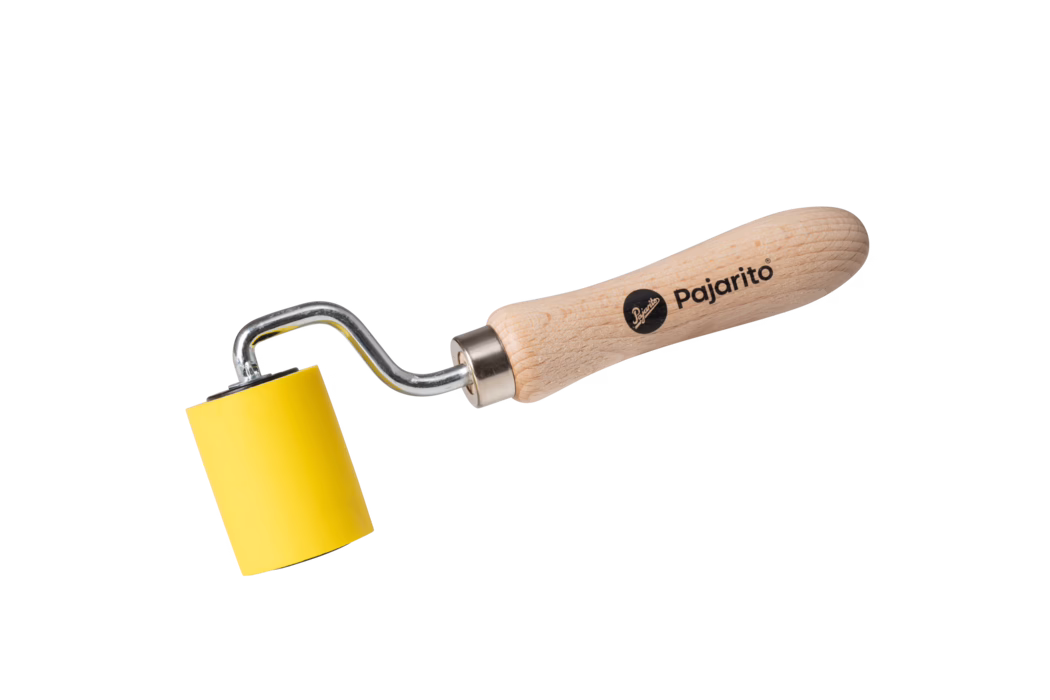 Hochauflösende Produktaufnahme eines kleinen Handrollers vor rein weißem Hintergrund. Das Werkzeug hat einen glatten, hellen Buchenholzgriff, der mit dem Markennamen „Pajarito“ und einem runden schwarzen Logo bedruckt ist. Eine verchromte Metallwelle mit charakteristischer gewinkelter Form verbindet den Griff mit einer zylindrischen gelben Gummi- oder Schaummrolle. Die Rolle ist leuchtend gelb, von kleinem bis mittlerem Durchmesser, mit planem Ende und gleichmäßiger Oberfläche. Die Komposition zeigt das Werkzeug diagonal im Bild von unten links nach oben rechts und stellt Details klar dar: sichtbare Holzmaserung am Griff, dezente Reflexe auf dem Metall und weiche Schatten unter Rolle und Griff. Die Beleuchtung ist gleichmäßig und neutral, betont Farben und Materialien ohne starke Kontraste. Geeignet für E‑Commerce, Produktkataloge oder Anleitungen; vermittelt Größe, Material, Markenkennzeichnung und Einsatzbereich zum Glätten, Andrücken oder gleichmäßigen Aufbringen von Druck, Klebstoffen, Tapeten oder ähnlichen Oberflächen.