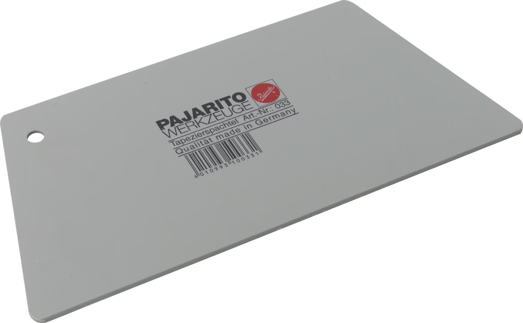 Pajarito_Dummy_Wallpaper scraper trapezoid_034821_2021-02 Grauer rechteckiger Kunststoff-Tapezierspachtel liegt diagonal auf weißem Hintergrund, mit abgerundeten Ecken und Aufhängeloch an einer kurzen Seite. Mittig schwarzer Aufdruck 'PAJARITO WERKZEUGE' mit der Produktangabe 'Tapezierspachtel Art.-Nr.: 033 Qualität made in Germany' und einem Strichcode darunter. Glattes, flaches Blatt zum Glätten von Tapeten und Verteilen von Kleister.