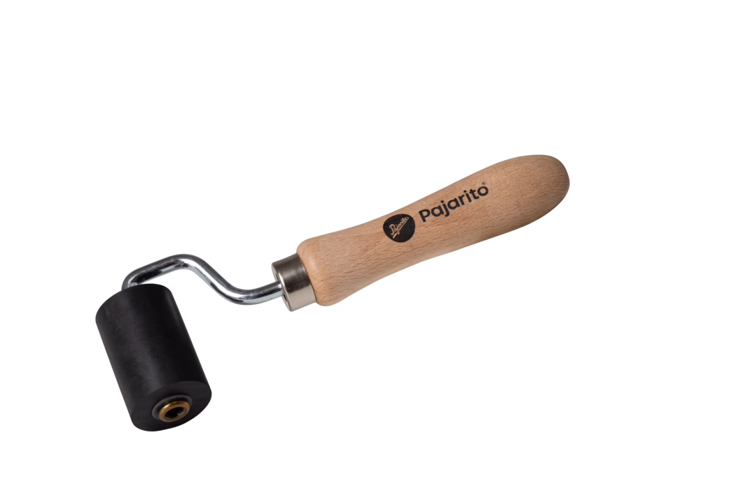 Ein kleiner Handroller mit glattem Holzgriff, auf dem "Pajarito" steht, einer verchromten, gebogenen Metallachse und einer zylindrischen schwarzen Gummiwalze. Das Werkzeug dient zum Andrücken von Stößen, Glätten von Klebstoffen und Vinyl sowie zum Entfernen von Luftblasen bei Tapezier-, Bodenbelags- oder Bastelarbeiten. Auf weißem Hintergrund fotografiert, zeigt der Holzgriff deutliche Maserung und eine Metallhülse verbindet ihn mit der Walze; handliche Größe für präzise Arbeiten.