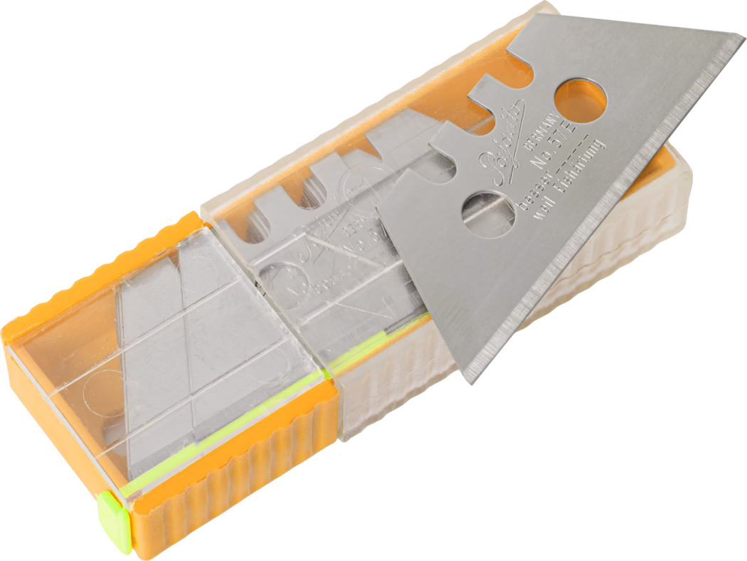 Pajarito_Dummy_Trapezoid blades large hole Performance Line_168595_2021-11 Eine Kunststoff-Box mit mehreren dreieckigen Abbrechklingen für Universalmesser. Der transparente und orangefarbene Kunststoffbehälter enthält gestapelte Edelstahlklingen mit Aussparungen und runden Löchern; eine Klinge liegt oben und zeigt die scharfe abgeschrägte Schneide sowie eingeprägte Schriftzüge. Das Bild ist gut ausgeleuchtet vor weißem Hintergrund und zeigt die Struktur der Kunststoffhülle und die reflektierenden Metallflächen in einer Nahaufnahme in leichter Schrägsicht.