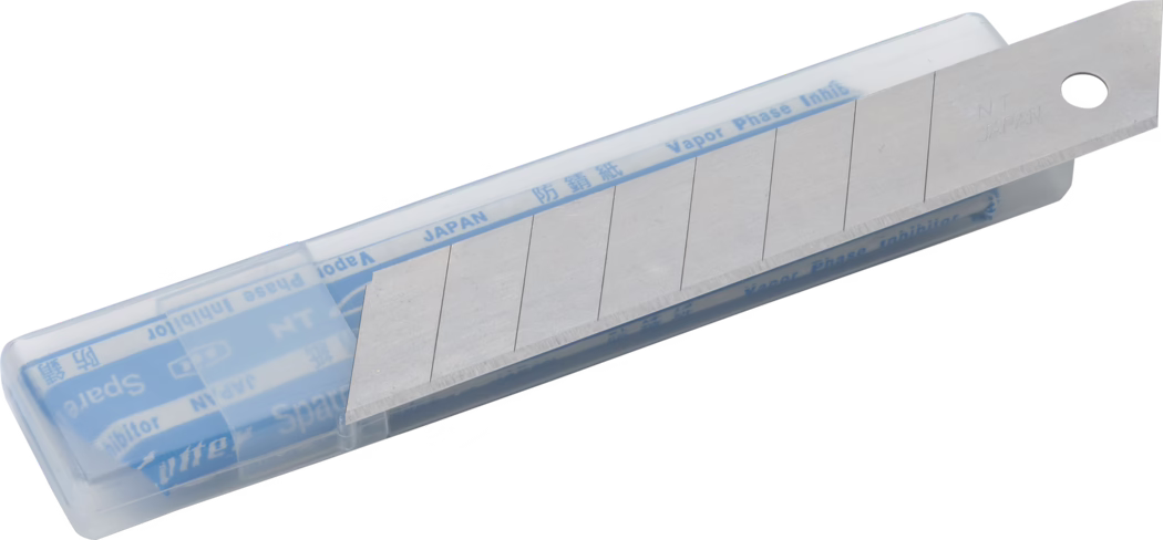 Ein transparenter Kunststoffbehälter mit einem Ersatzklingenstreifen für Abbrechklingen. Die silberne Stahlklinge ist teilweise vorgeschoben und zeigt mehrere eingeritzte Bruchsegmente; ein Segment ist abgeschrägt und freigelegt. In der Hülle liegt blaues Schutzpapier mit den Aufdrucken 'JAPAN' und 'Vapor Phase Inhibitor'. Der metallene Klingensteg ist mit 'NT JAPAN' geprägt und besitzt ein rundes Loch am Ende. Der Kunststoffspender liegt schräg auf weißem Hintergrund.